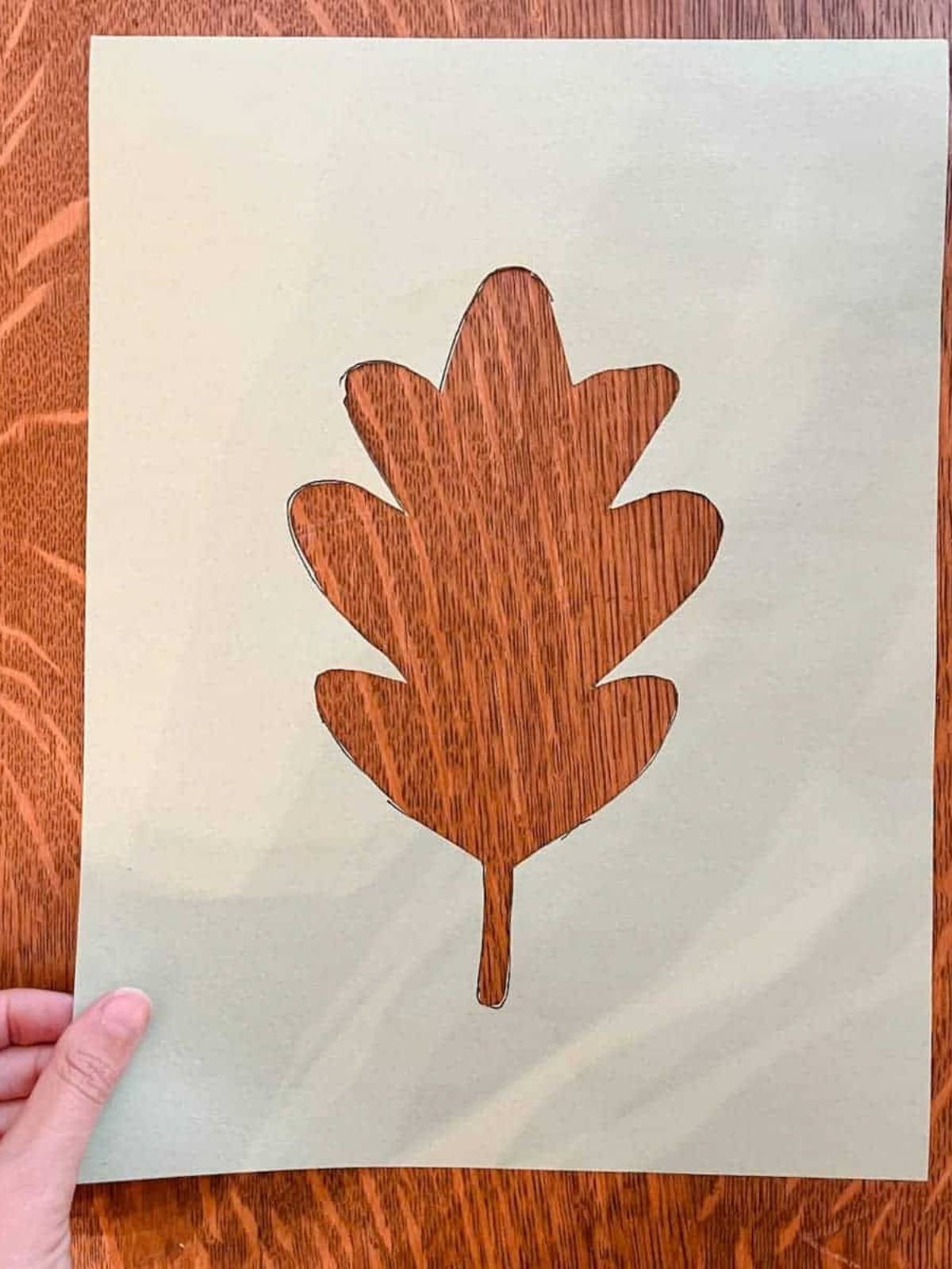 cut out leaf outline out of inside of construction paper with hand holding corner of paper.