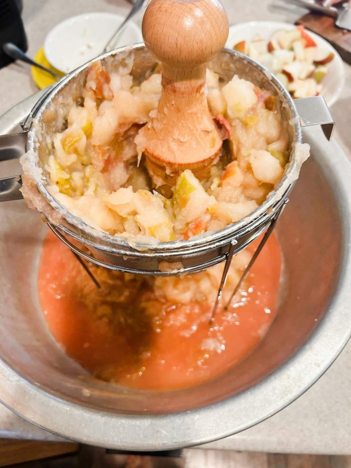 cooked apples in chinios with wooden pestile pushing the sauce through the strainer at the bottom of the chinois.