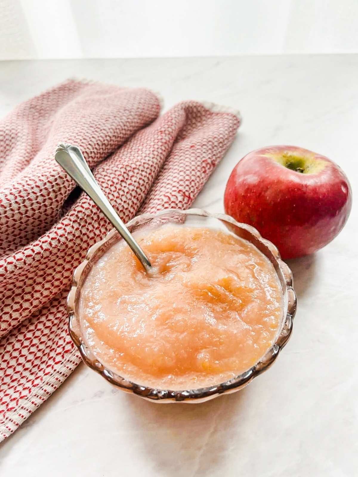 finished applesauce in bowl with spoon in bowl next to red tea towel and apple.