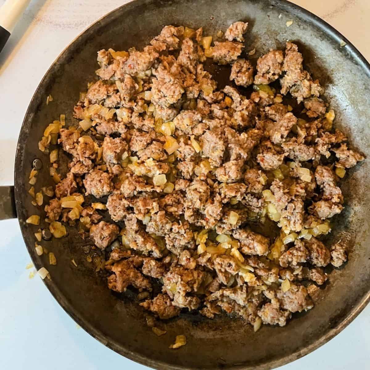 Browned Italian sausage in a skillet with onions.