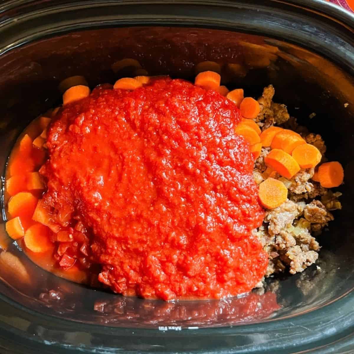 Tomatoes, carrots and sausage and other ingredients dumped into the crockpot.