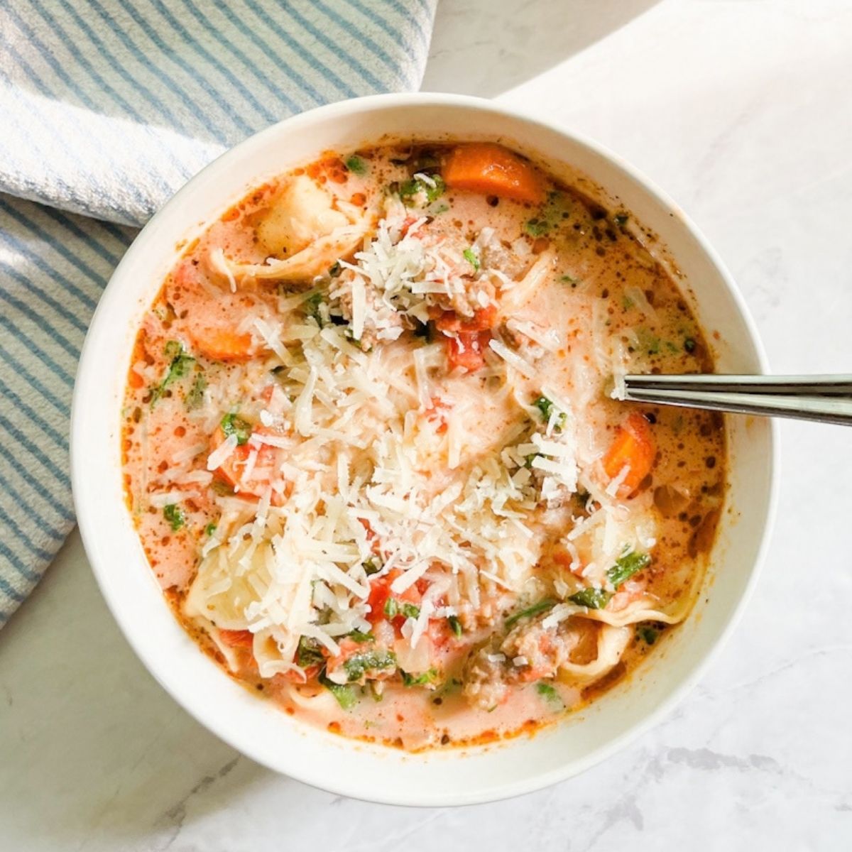 Finished tortellini soup with grated parmesan on top next to a towel on the counter.