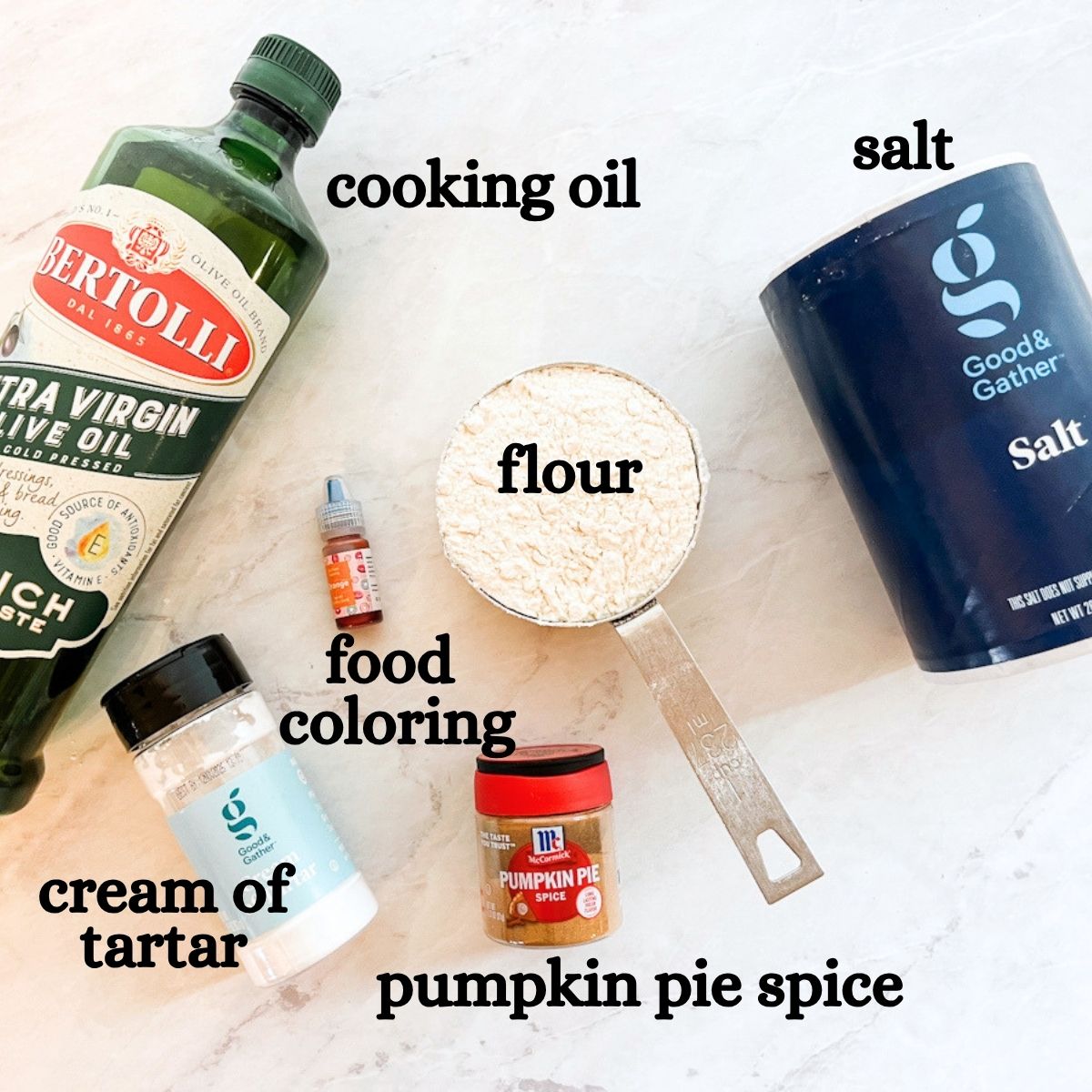 Ingredient shot of the oil, salt, flour, cream of tartar, food coloring and pumpkin pie spice sitting on the counter.