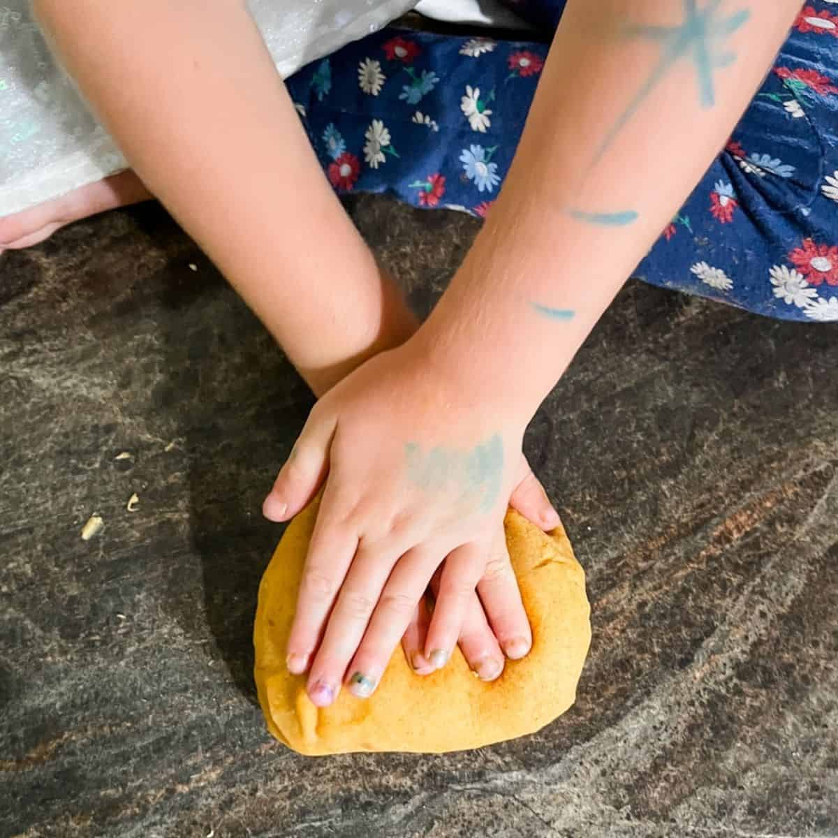 Child's hands kneading the pumpkin pie playdough on a countertop.