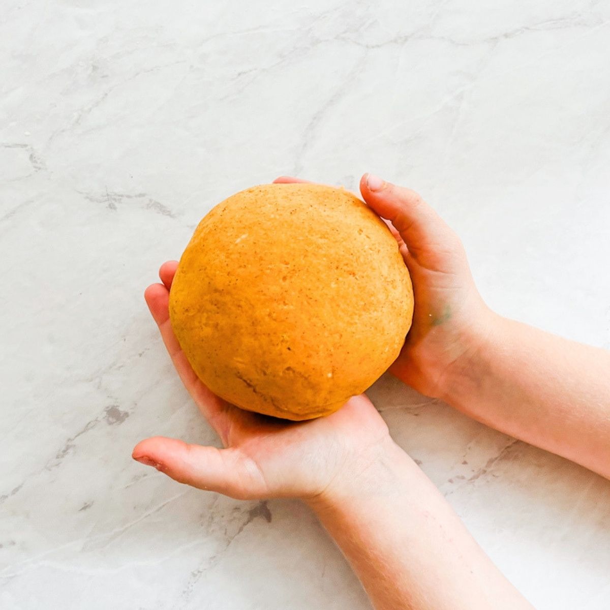 Child's hands with the dough ball of pumpkin spice playdough.