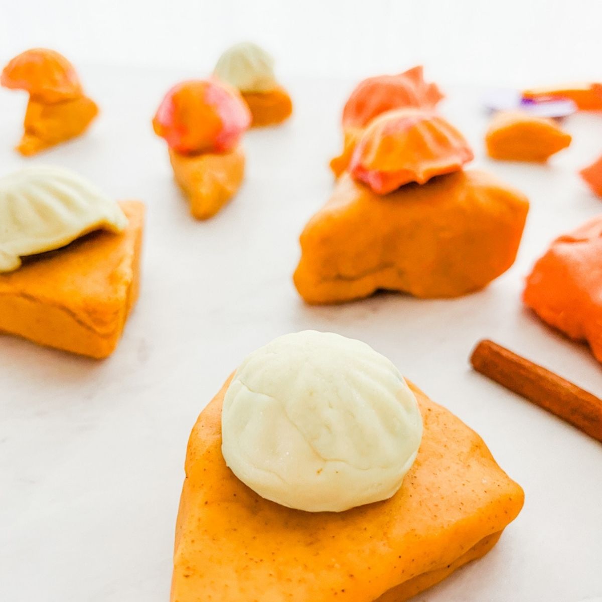 Lots of pumpkin spice playdough pies sitting on a white counter top.