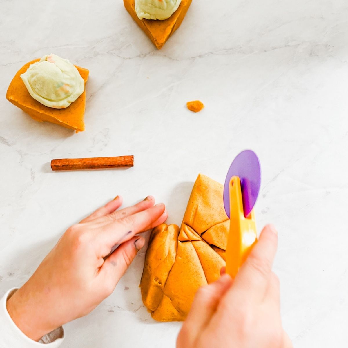 Childs hands cutting pumpkin playdough into slices like a pie on the counter.