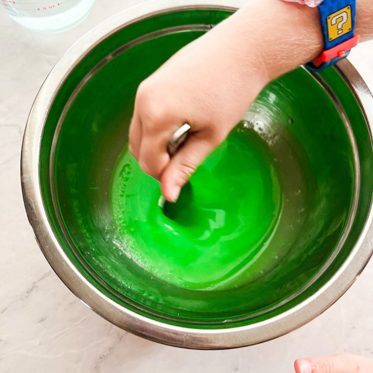 Hand stirring green substance in a large bowl.