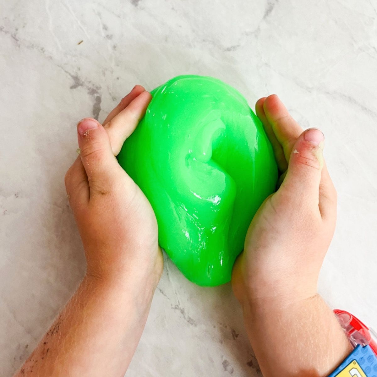 Child/s hands kneading the green glow in the dark slime on the counter.