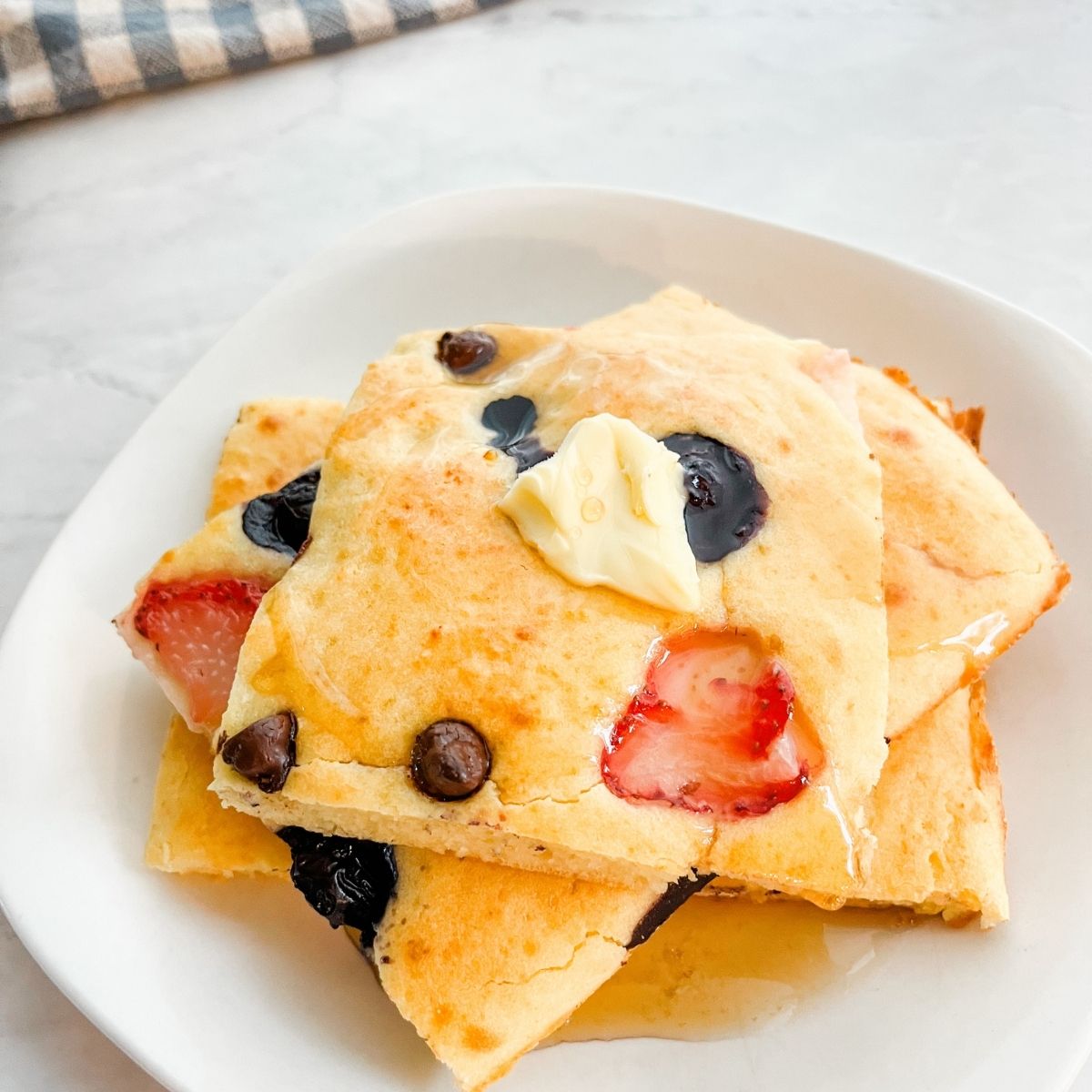 Fluffy sheet pan pancakes with blueberries and strawberries covered with maple syrup and butter.