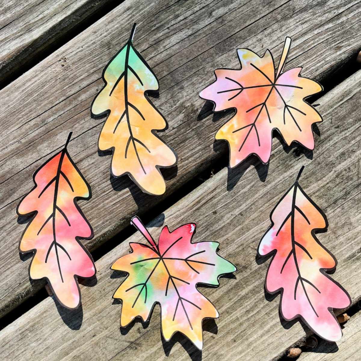 Five finished leaf templates with watercolor look and cut out sitting on a piece of wood.